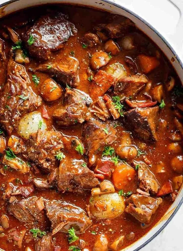 Boeuf Bourguignon servi dans un plat blanc et un bol, préparé dans une poêle.